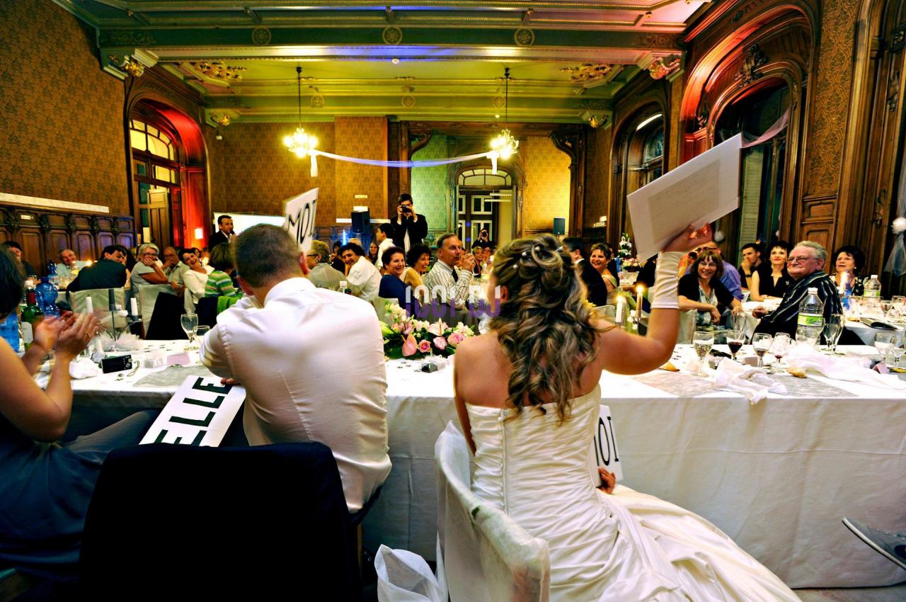 Des invités assis autour de tables décorées applaudissent lors d'une réception de mariage dans une salle élégante.