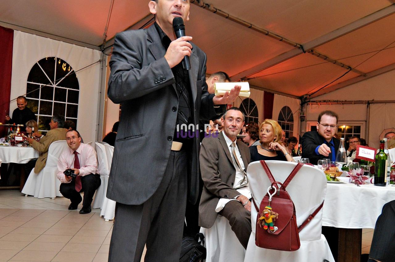 Un homme en costume parle au micro dans une salle sous tente, entouré de tables occupées par des convives.