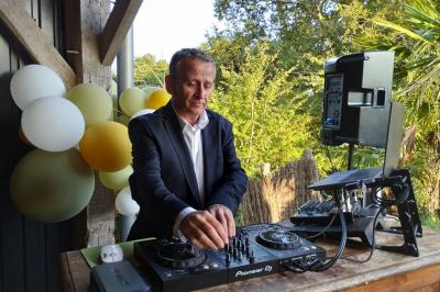 Un homme en costume utilise une table de mixage lors d'un événement en extérieur, avec des ballons en arrière-plan.