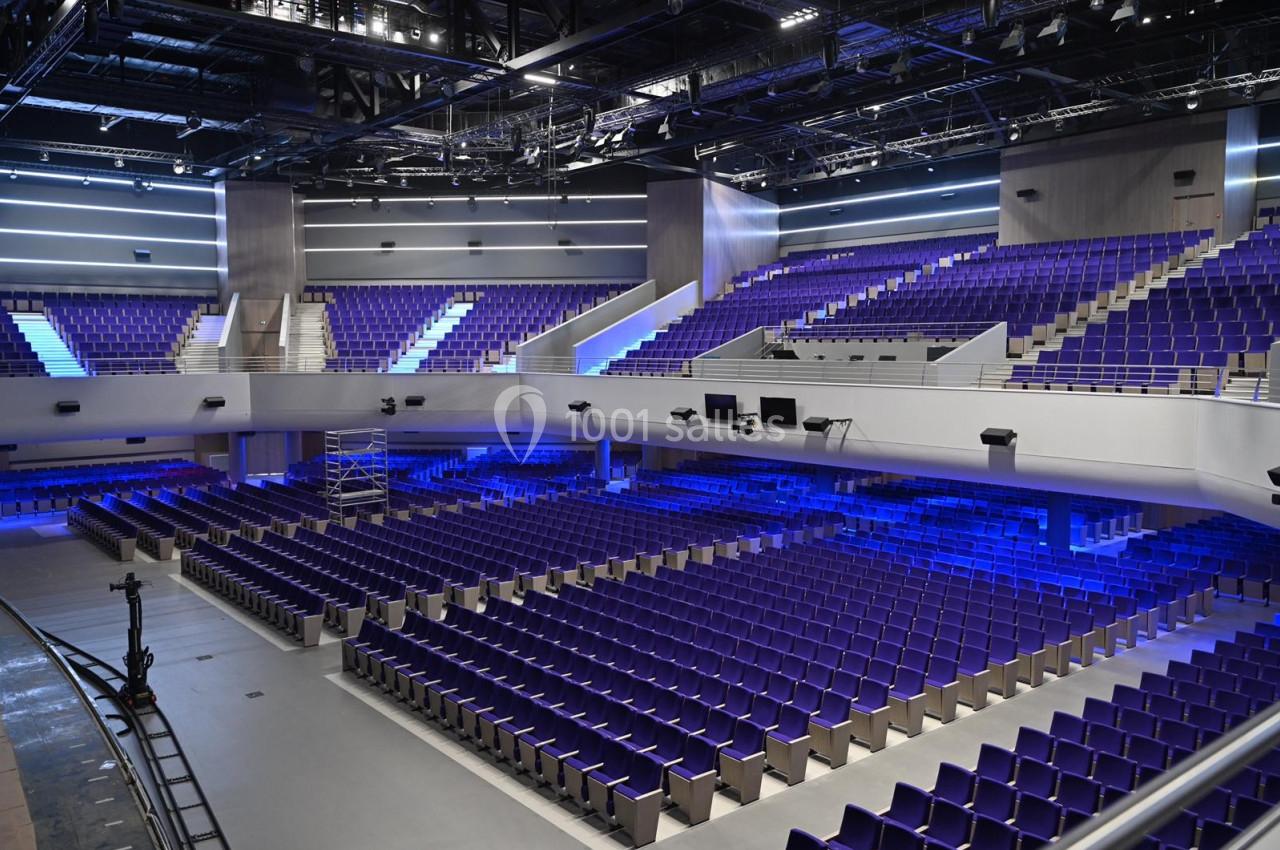 Salle de spectacle moderne avec des rangées de sièges violets et un éclairage bleu, vue depuis la scène.