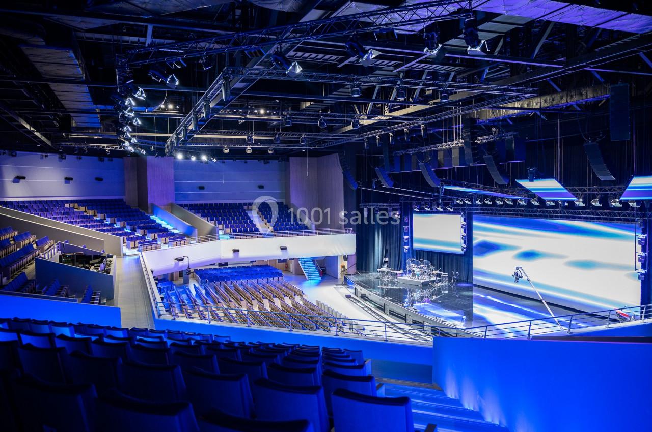 Salle de spectacle moderne avec scène équipée, éclairage professionnel et rangées de sièges vides en gradins.