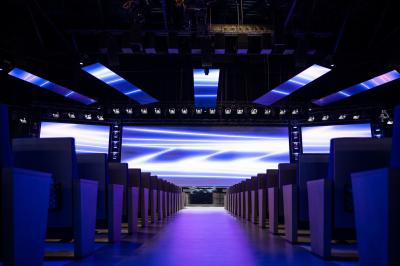 Vue aérienne d'un grand bâtiment moderne avec un parking rempli de voitures à l'avant et des arbres en arrière-plan.