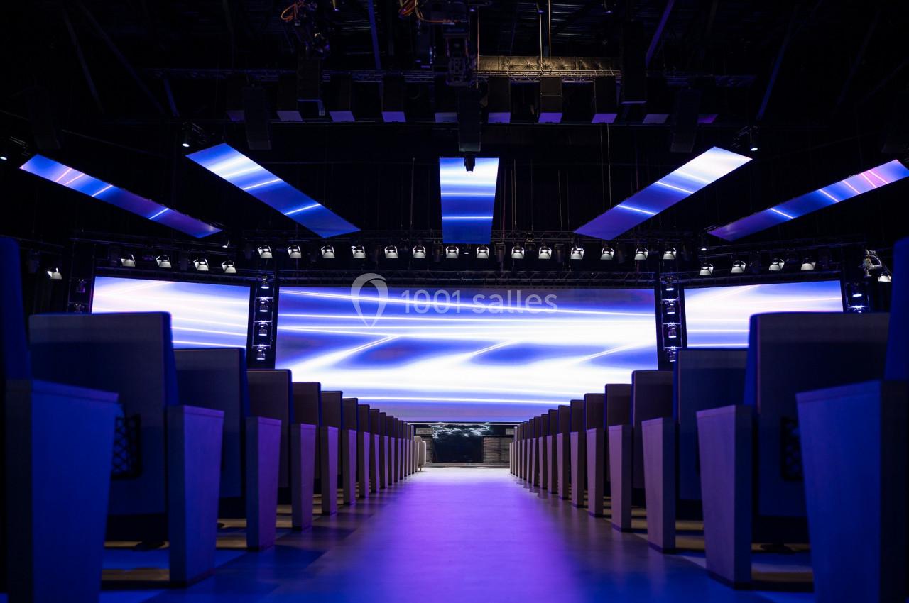 Salle de conférence moderne avec rangées de sièges et écrans lumineux affichant des motifs abstraits bleus.