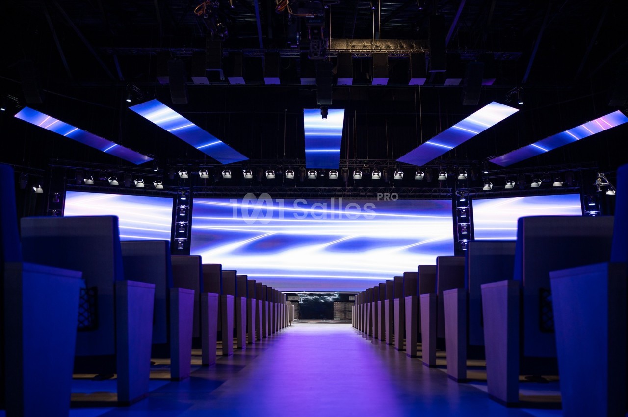 Salle de conférence moderne avec rangées de sièges et écrans lumineux affichant des motifs abstraits bleus.