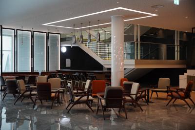 Vue aérienne d'un grand bâtiment moderne avec un parking rempli de voitures à l'avant et des arbres en arrière-plan.