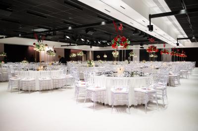 Vue aérienne d'un grand bâtiment moderne avec un parking rempli de voitures à l'avant et des arbres en arrière-plan.