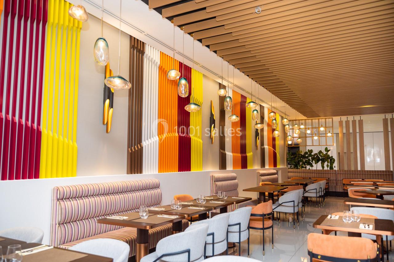 Salle de restaurant moderne avec tables dressées, banquettes rayées, chaises rembourrées et décor coloré aux murs.