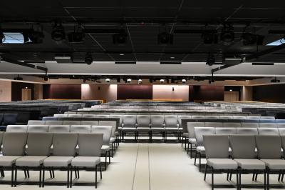 Vue aérienne d'un grand bâtiment moderne avec un parking rempli de voitures à l'avant et des arbres en arrière-plan.