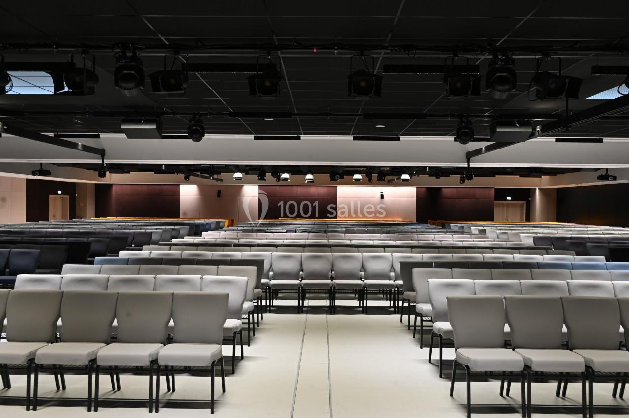 Salle de conférence vide avec rangées de chaises alignées et éclairage suspendu au plafond.