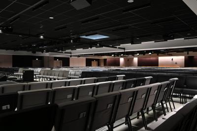 Vue aérienne d'un grand bâtiment moderne avec un parking rempli de voitures à l'avant et des arbres en arrière-plan.