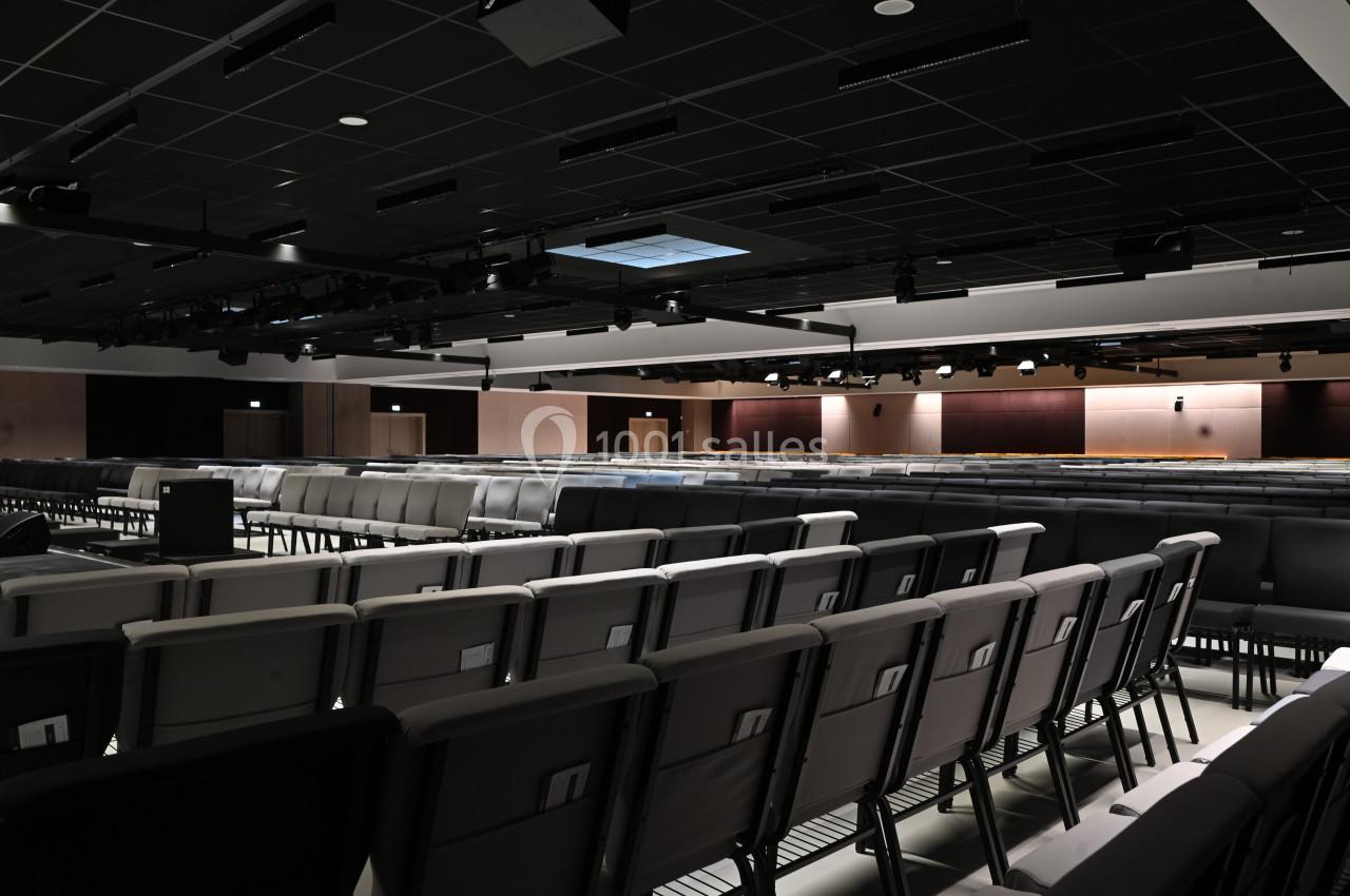 Salle de conférence vide avec rangées de sièges alignés et plafond équipé de luminaires.
