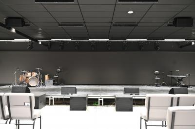 Vue aérienne d'un grand bâtiment moderne avec un parking rempli de voitures à l'avant et des arbres en arrière-plan.