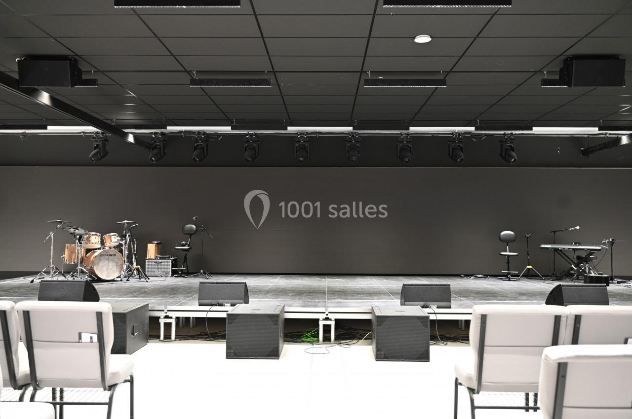 Scène vide avec instruments de musique, éclairages suspendus et chaises disposées au premier plan.