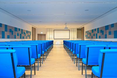 Vue aérienne d'un grand bâtiment moderne avec un parking rempli de voitures à l'avant et des arbres en arrière-plan.