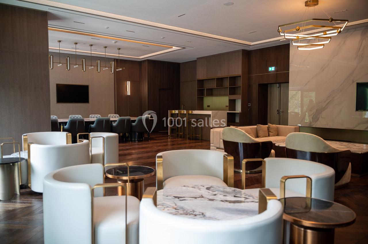Salle moderne avec fauteuils blancs, tables en marbre, parquet en bois sombre et éclairage design.