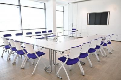 Vue aérienne d'un grand bâtiment moderne avec un parking rempli de voitures à l'avant et des arbres en arrière-plan.