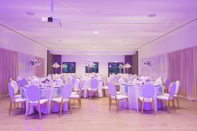 Vue aérienne d'un grand bâtiment moderne avec un parking rempli de voitures à l'avant et des arbres en arrière-plan.