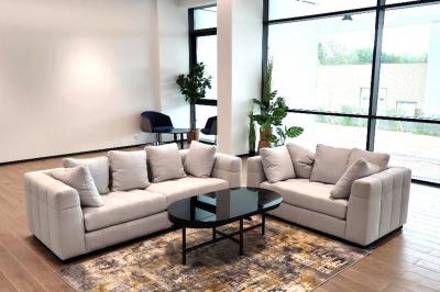 Vue aérienne d'un grand bâtiment moderne avec un parking rempli de voitures à l'avant et des arbres en arrière-plan.