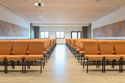 Vue aérienne d'un grand bâtiment moderne avec un parking rempli de voitures à l'avant et des arbres en arrière-plan.