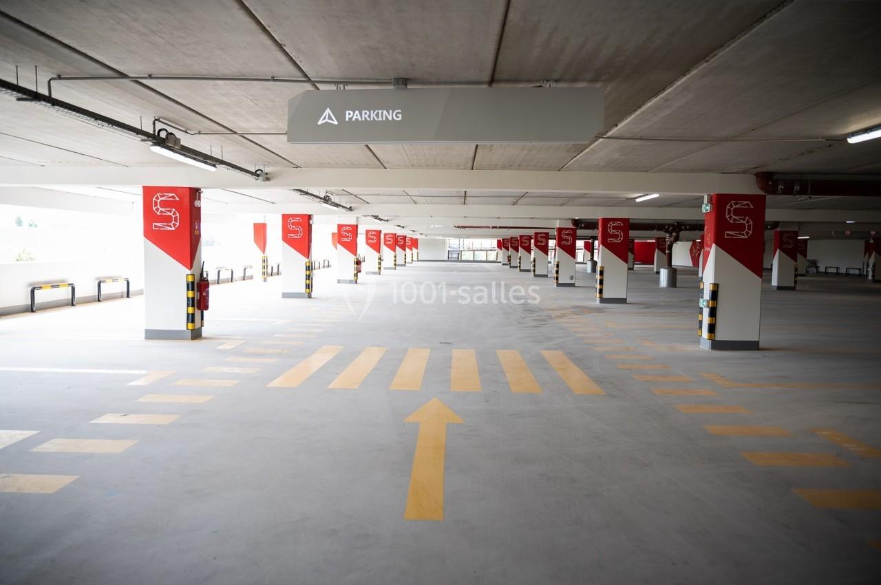Parking couvert vide avec marquages au sol jaunes et panneaux rouges indiquant les emplacements.