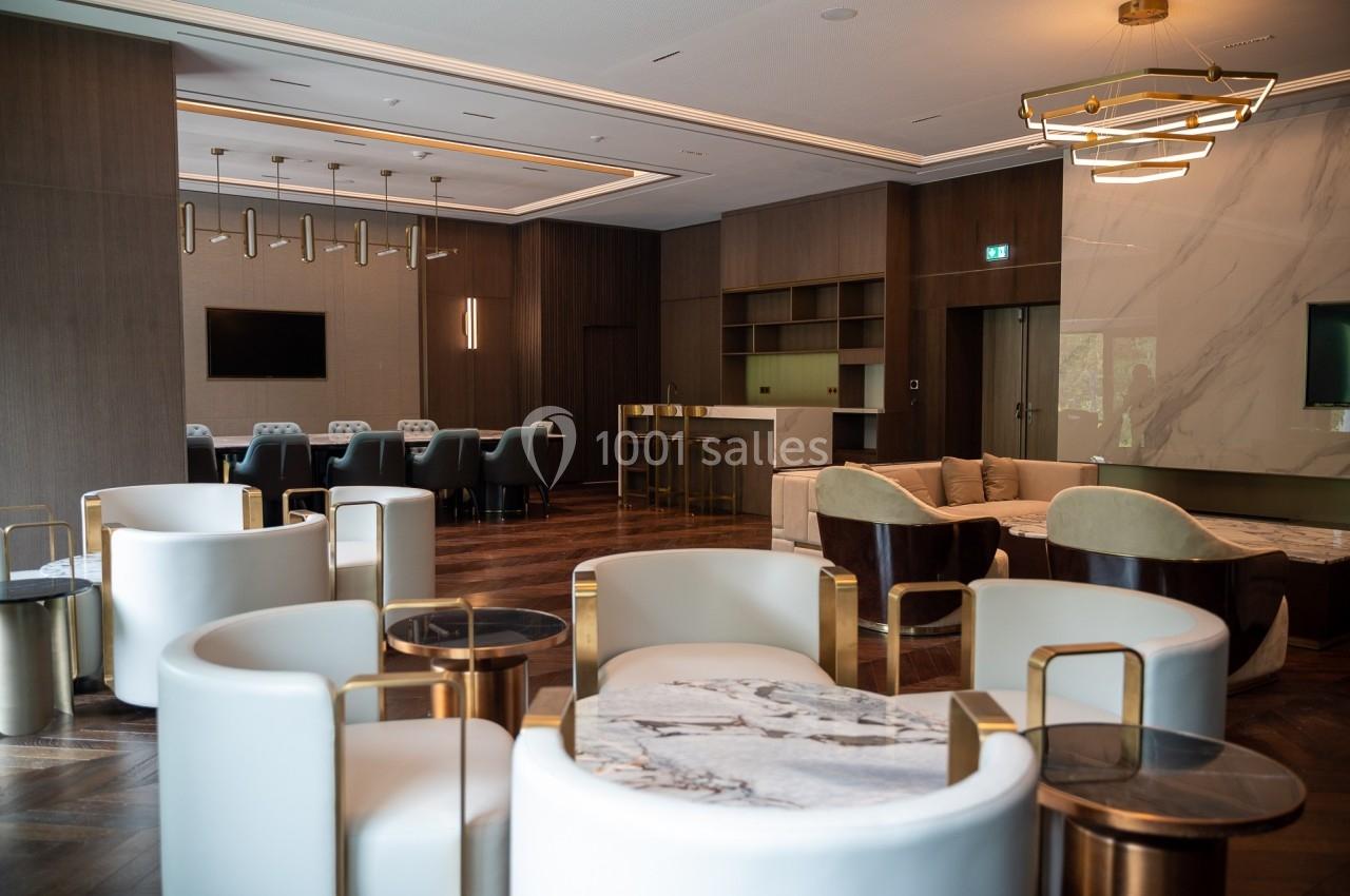 Salle moderne avec mobilier élégant, fauteuils blancs, tables en marbre, parquet en bois et éclairage design.