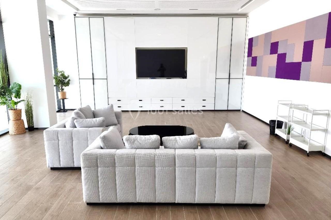 Salon moderne avec canapés gris, table basse noire, écran mural et décoration murale géométrique colorée.