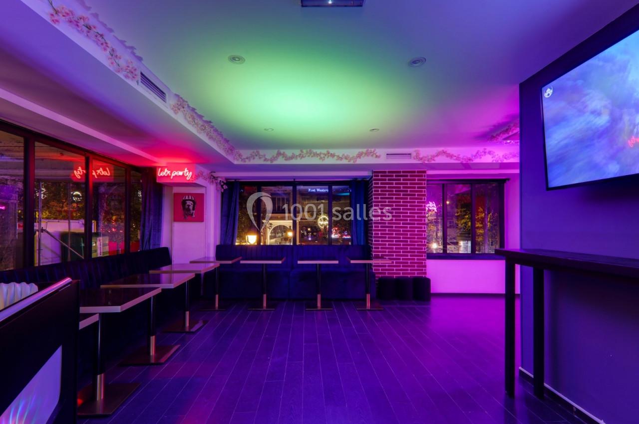 Salle lumineuse avec banquettes, tables et éclairage coloré, donnant sur des fenêtres avec vue nocturne.