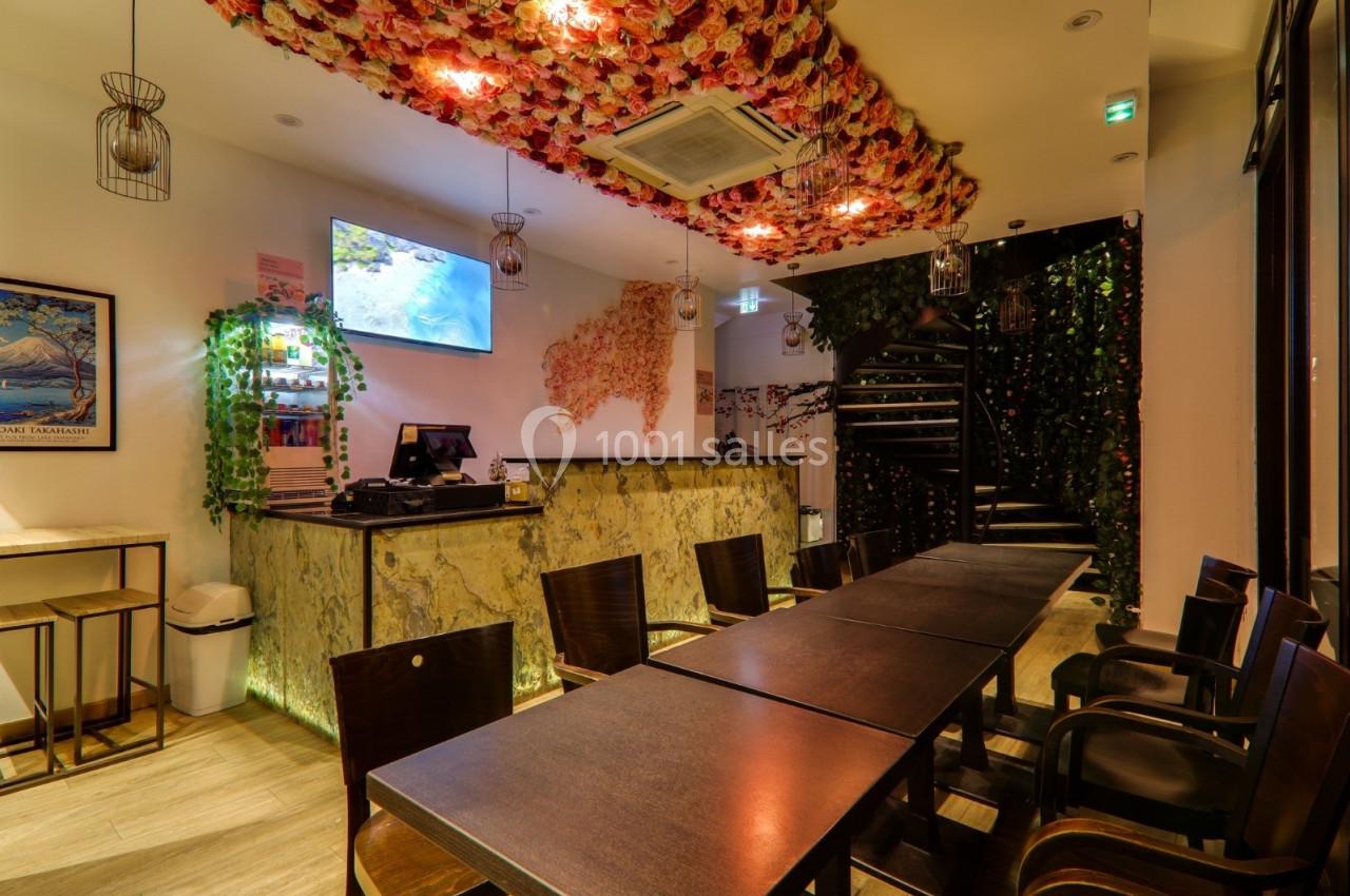 Salle de restaurant avec plafond décoré de fleurs, comptoir en marbre, tables en bois et escalier menant à l'étage.