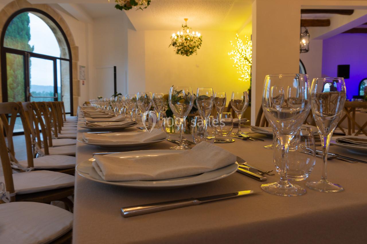 Salle de réception élégamment décorée avec une longue table dressée, des assiettes, verres et serviettes.