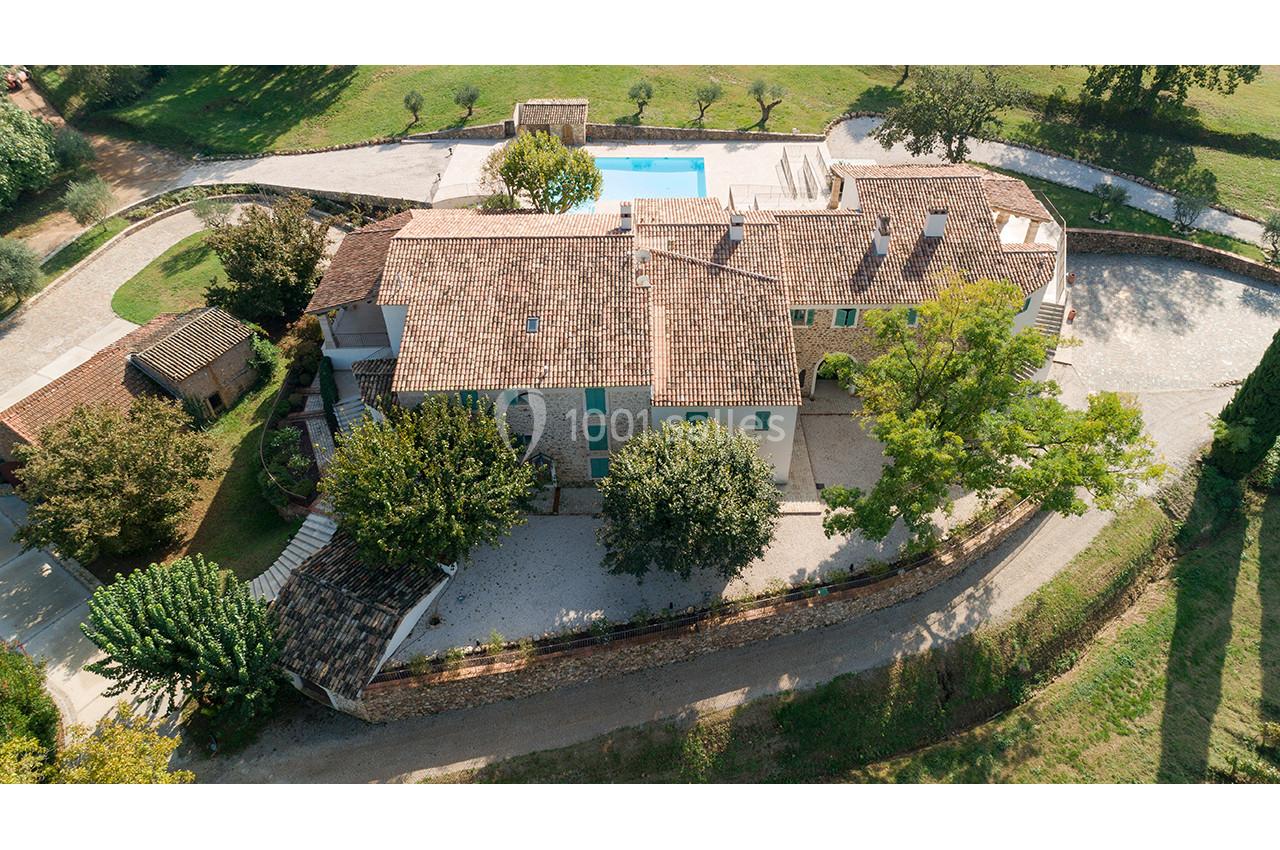 Vue aérienne d'une maison en pierre avec toit en tuiles, entourée d'arbres, d'une piscine et d'un chemin en gravier.