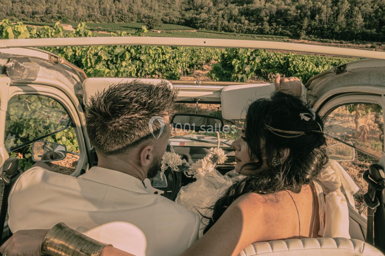 Un couple assis dans une voiture décapotable, entouré de vignes et de végétation sous une lumière douce.