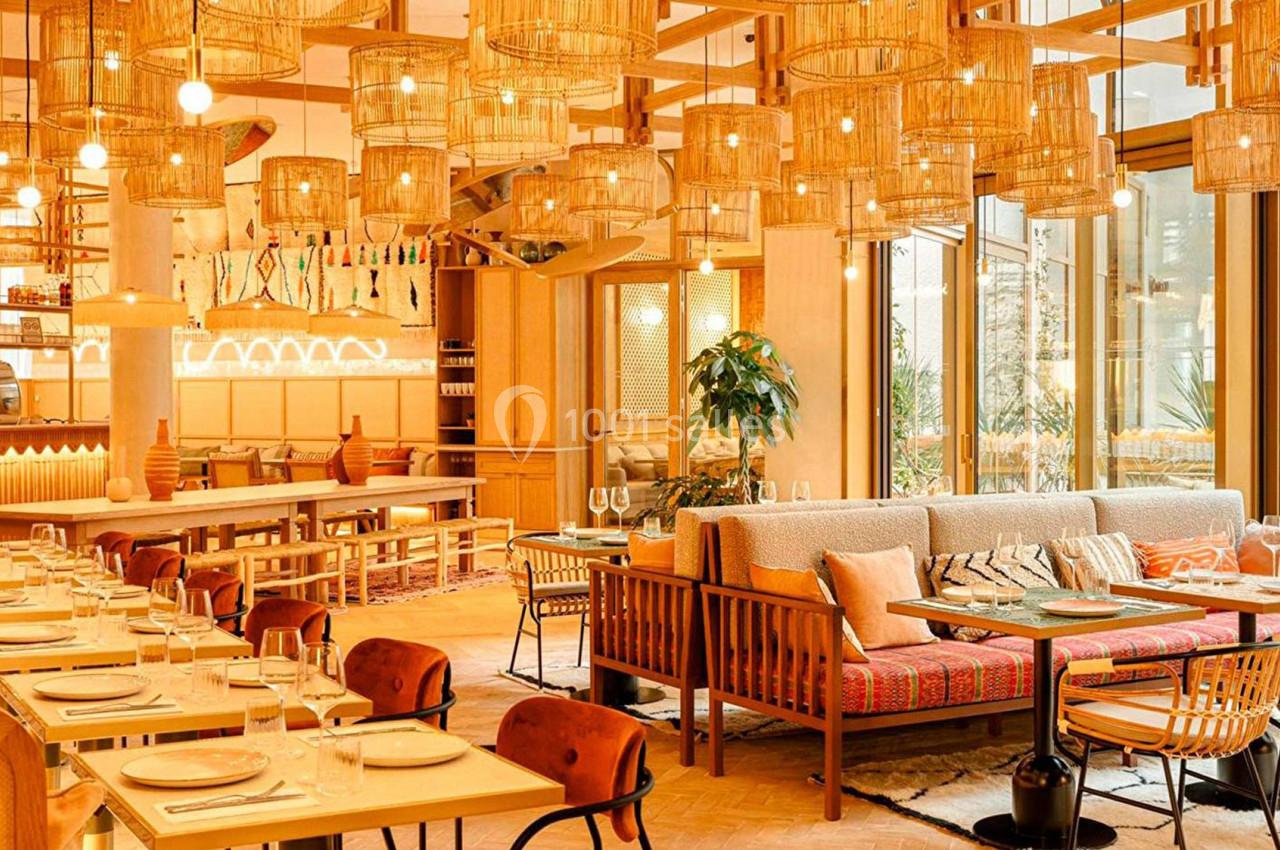 Salle de restaurant lumineuse avec mobilier en bois, lampes suspendues en osier et tables dressées.