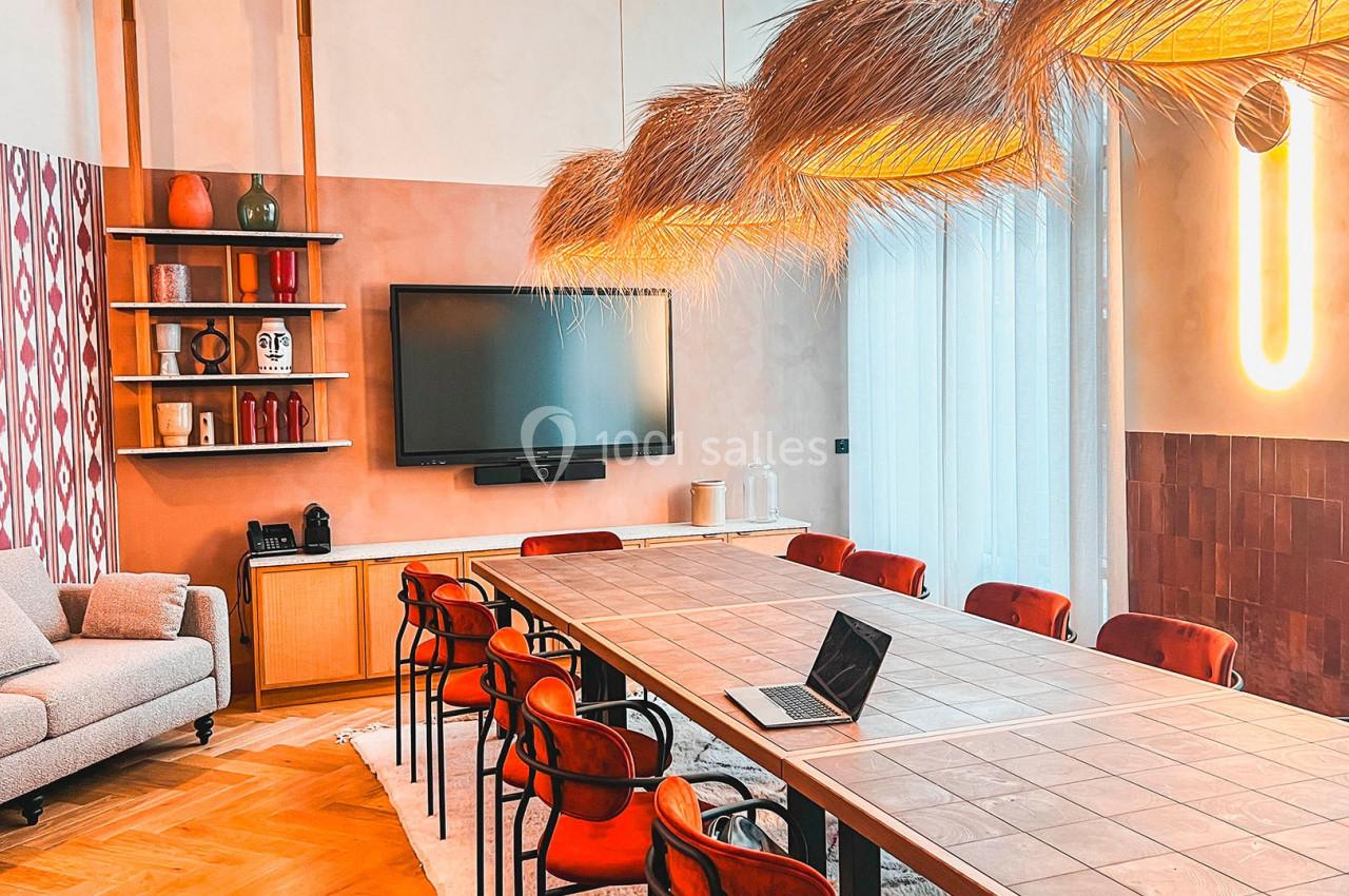 Salle de réunion lumineuse avec une grande table, des chaises rouges, un écran mural et des décorations modernes.