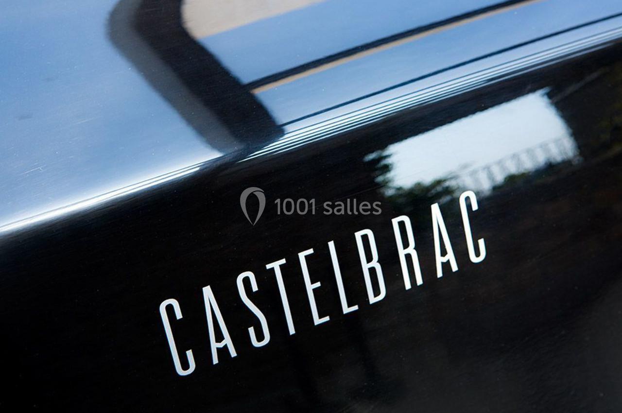 Texte ’Castelbrac’ inscrit sur une surface noire brillante, avec un reflet et un arrière-plan flou.