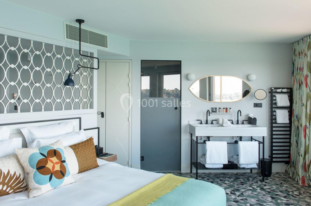 Chambre lumineuse avec lit double, tête de lit décorative, salle de bain attenante et sol en carreaux géométriques.