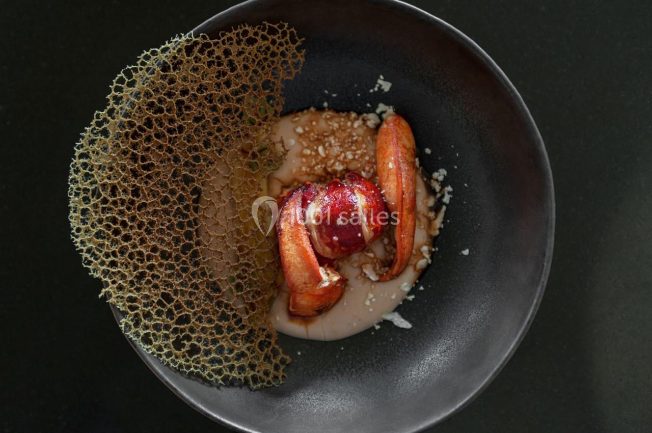 Assiette gastronomique avec homard, sauce crémeuse, crumble et tuile décorative sur fond noir.