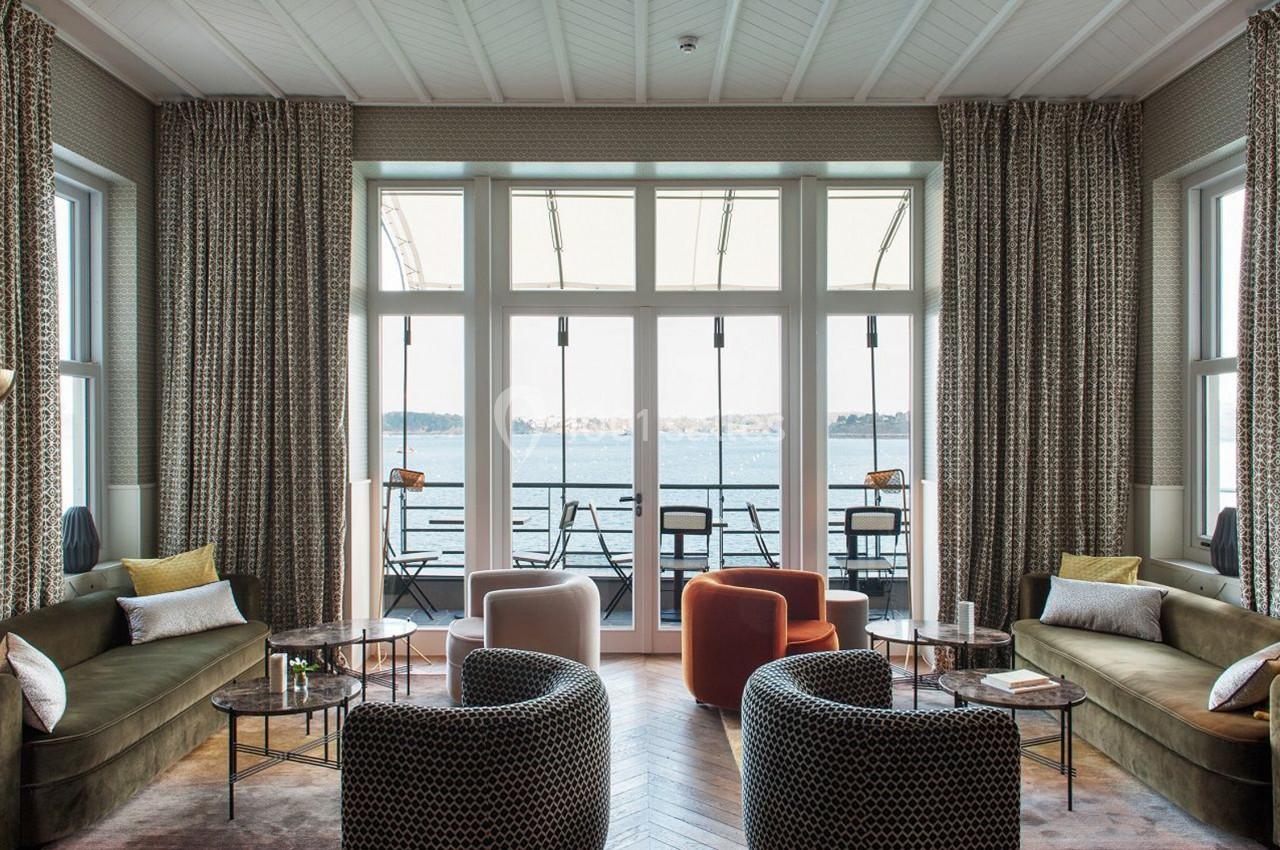 Salon lumineux avec grandes baies vitrées donnant sur une terrasse et une vue sur un plan d'eau.