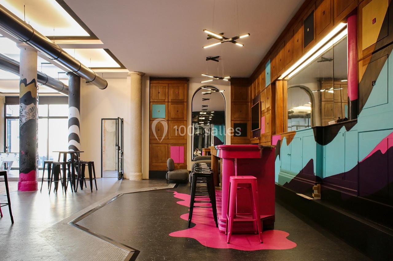 Espace intérieur moderne avec comptoir rose, tabourets, murs colorés et mobilier industriel.