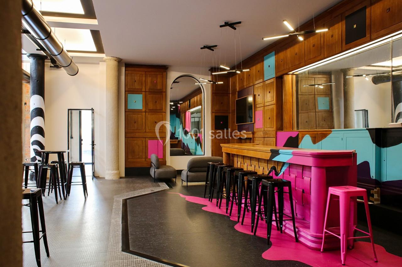 Espace intérieur moderne avec bar rose, tabourets noirs, murs en bois et décorations colorées.