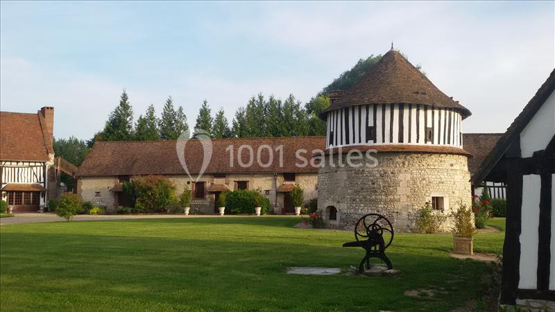 Bâtiments traditionnels à colombages et tour en pierre dans un jardin verdoyant par une journée ensoleillée.