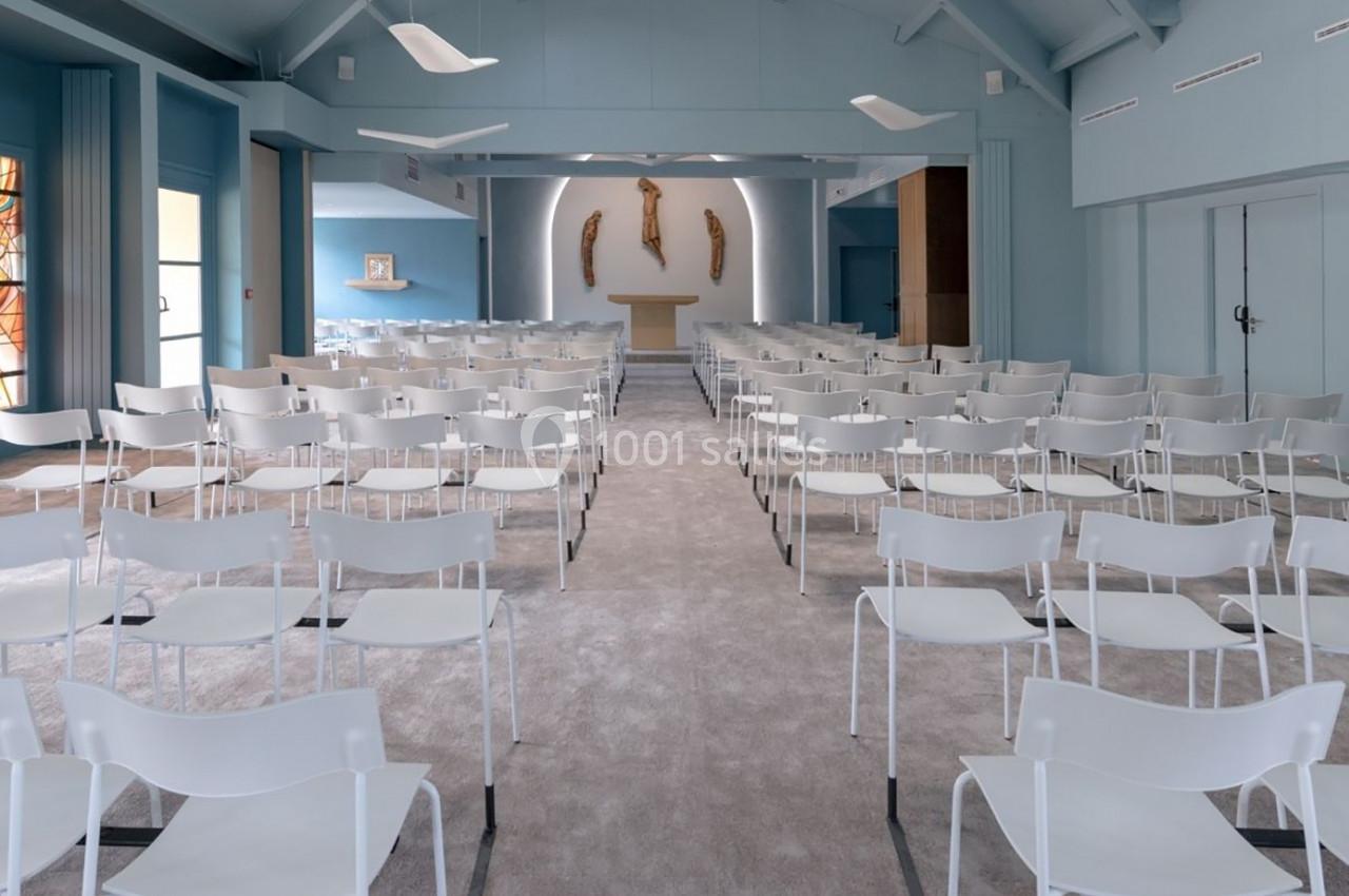 Salle de cérémonie moderne avec des chaises blanches alignées face à un autel et des sculptures murales.
