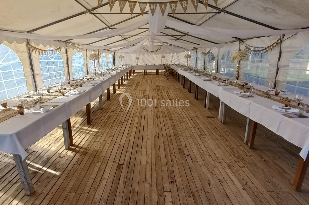 Salle de réception sous une tente avec de longues tables dressées et une bannière ’Just Married’ suspendue.