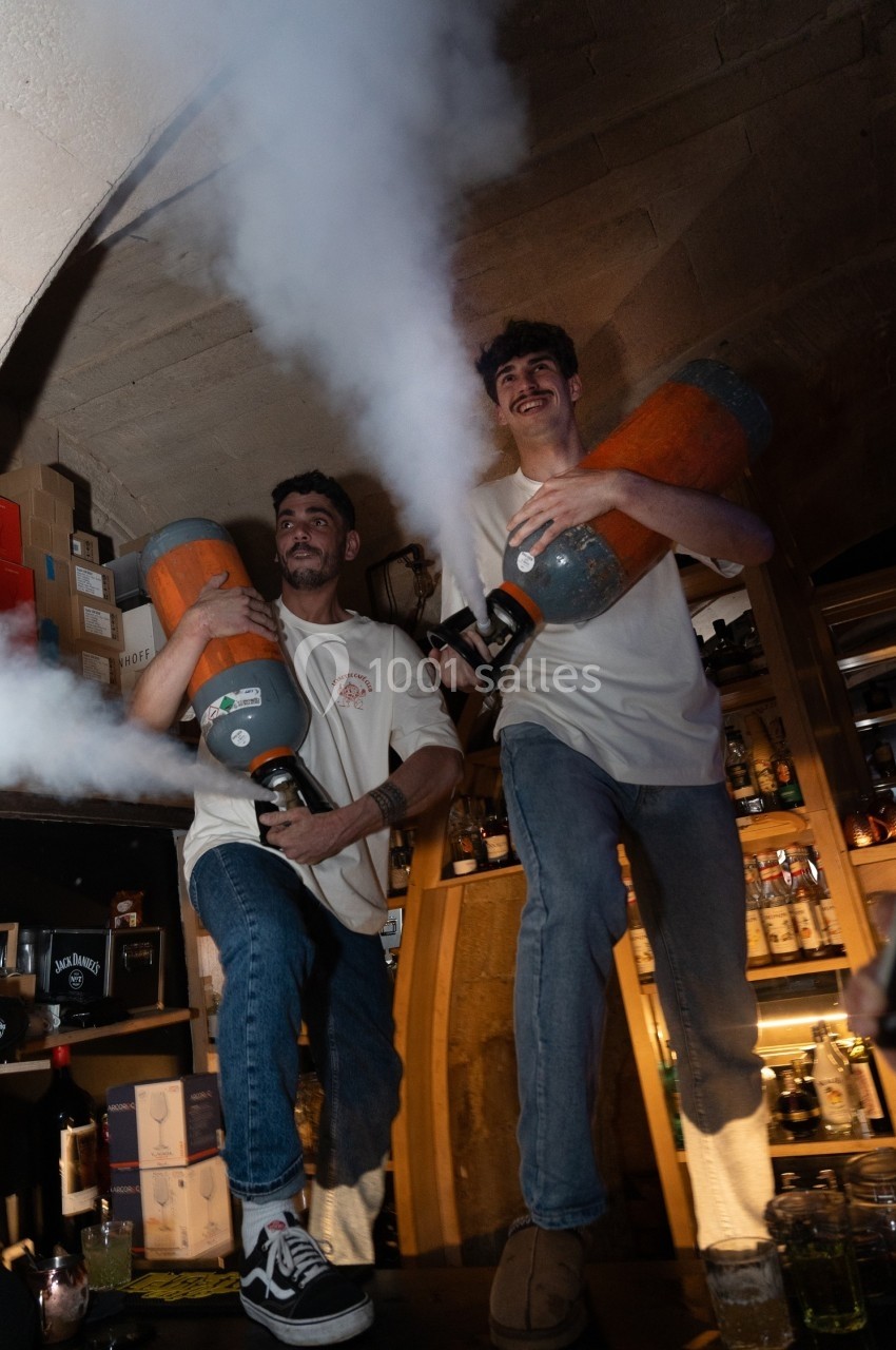 Deux hommes souriants sur un comptoir diffusent de la fumée avec des bonbonnes dans un bar.
