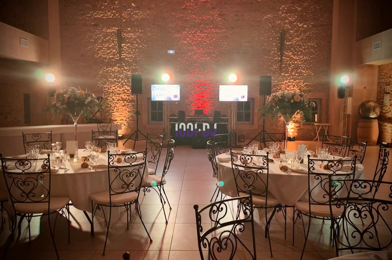 Salle de réception décorée avec des tables rondes dressées, chaises en fer forgé et éclairage chaleureux.