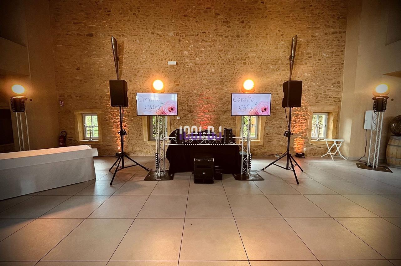 Installation de matériel de sonorisation et éclairage dans une salle en pierre avec deux écrans affichant un visuel.