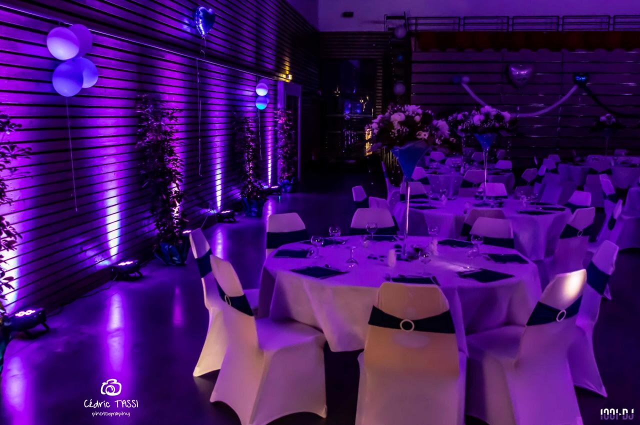 Salle décorée pour un événement, avec des tables rondes dressées et un éclairage violet créant une ambiance festive.