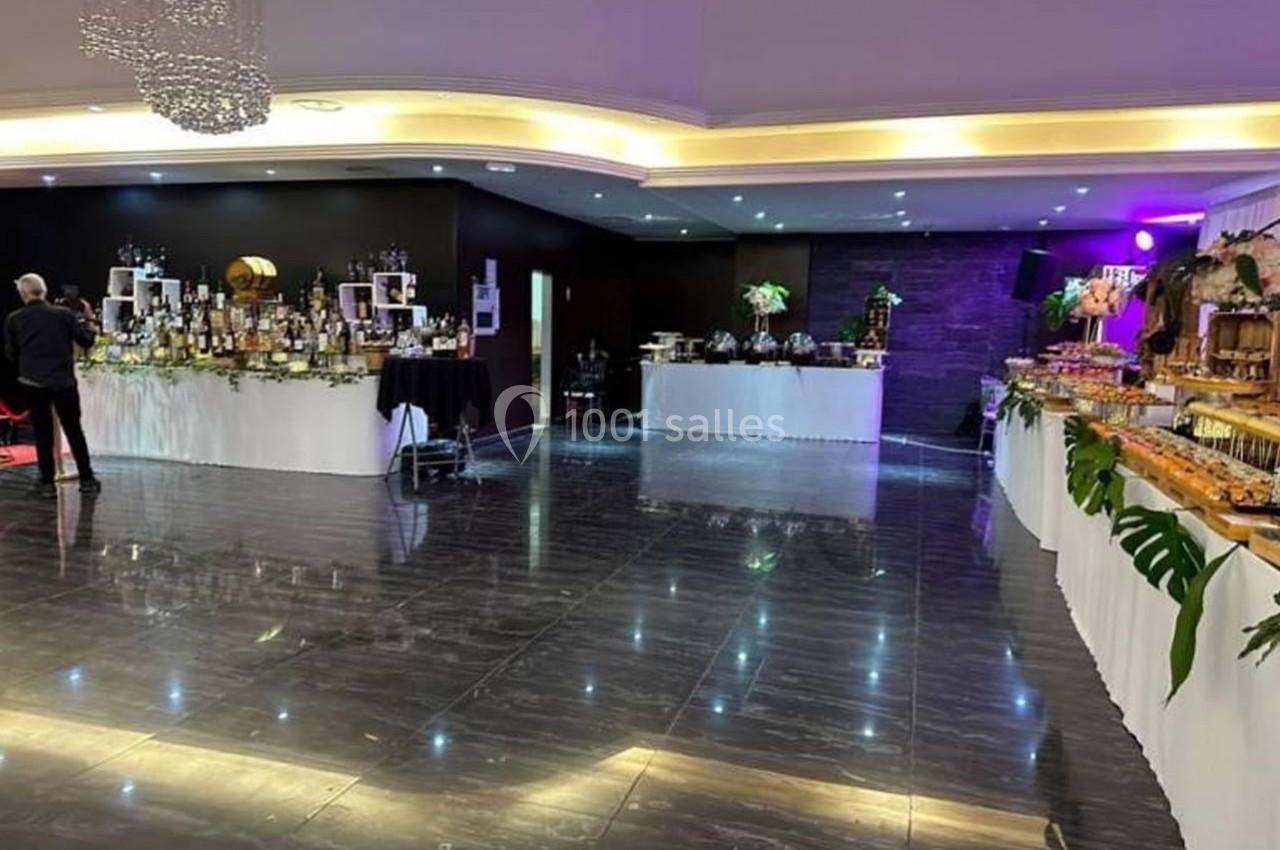 Salle de réception avec tables décorées et garnies de buffets variés, éclairage chaleureux et sol en marbre sombre.
