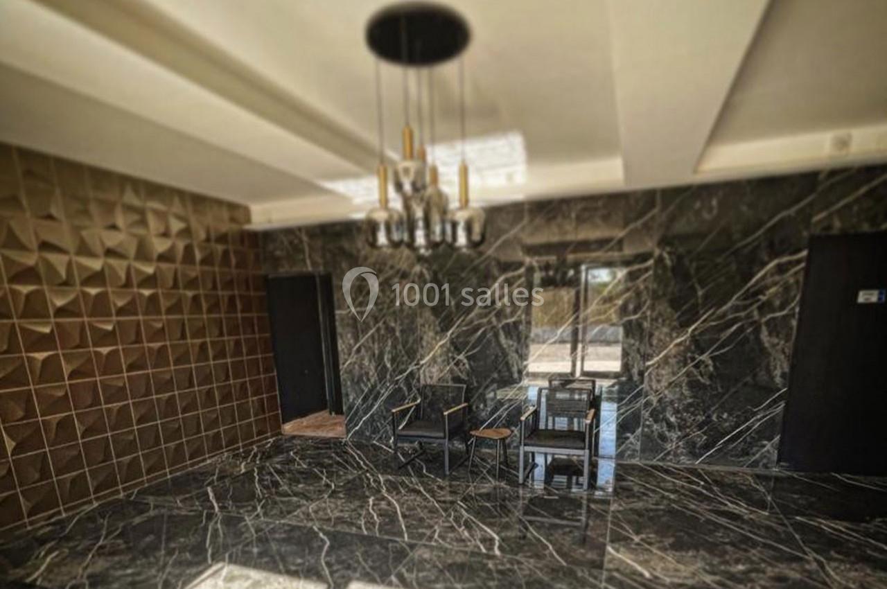 Salle moderne avec murs en marbre noir, un mur texturé doré, un lustre central et des chaises près d'une fenêtre.