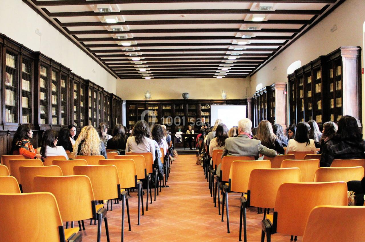 Salle de conférence avec des rangées de chaises orange, des participants assis et un écran de présentation au fond.