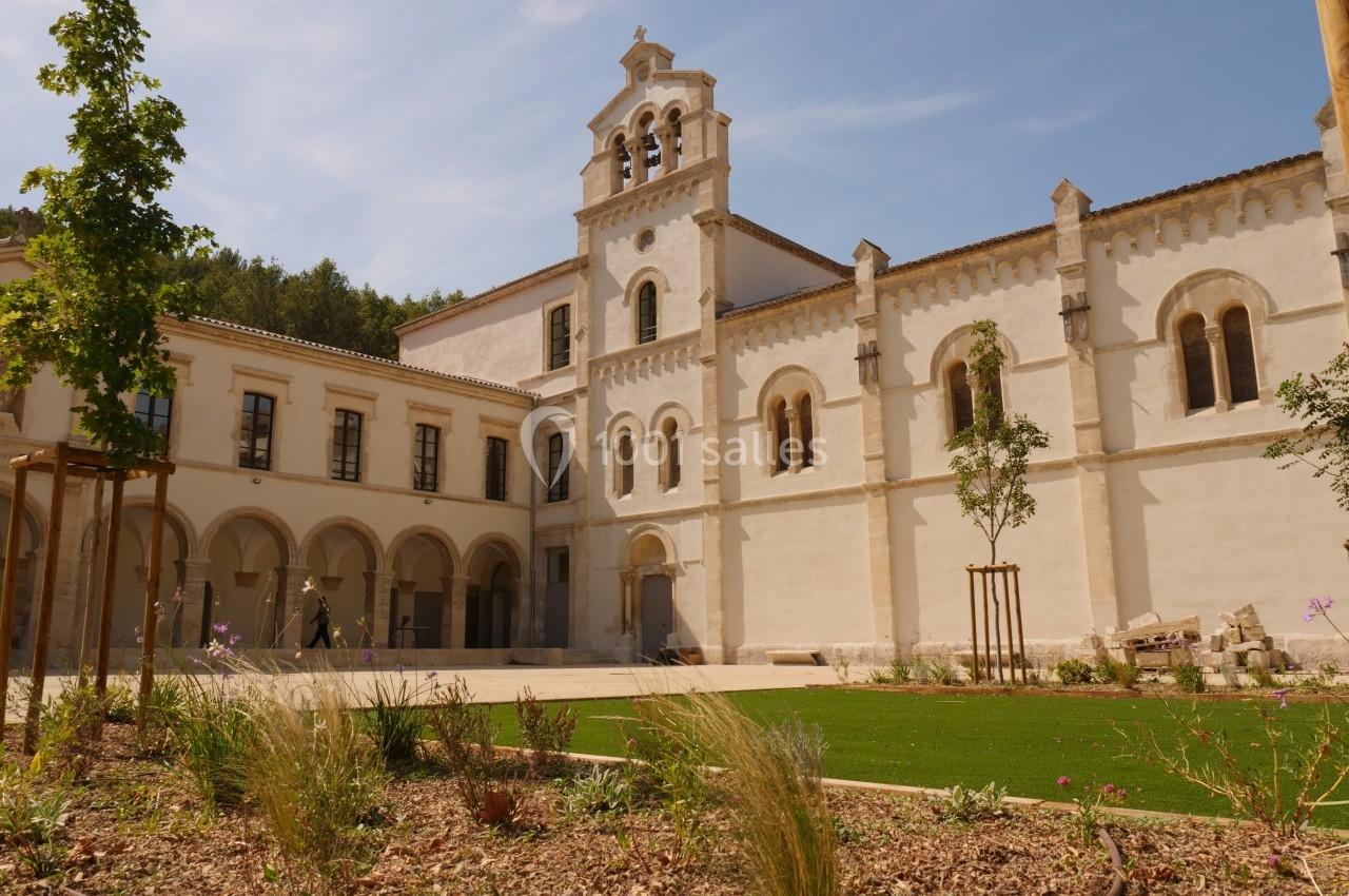 Façade d'un bâtiment historique en pierre blanche avec clocher, entouré d'un jardin paysager sous un ciel dégagé.
